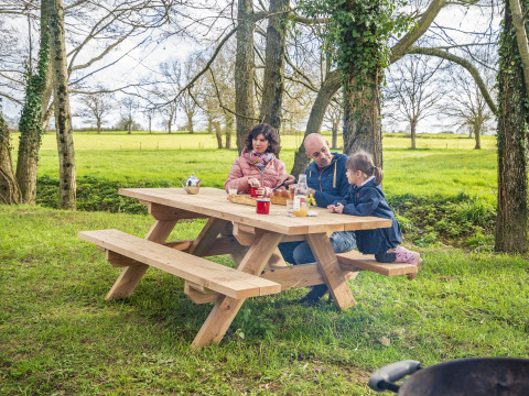 Famiglia seduta a un tavolo da picnic nel verde al BoerenBed L'Étable des Mauges en Anjou, Francia.