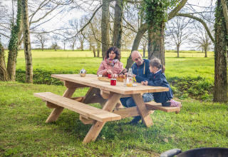 Gezin zit aan een houten picknickbank in het groen bij BoerenBed L'Étable des Mauges en Anjou.