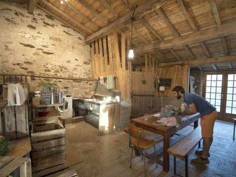 Uomo che lavora a un tavolo di legno in una cucina rustica con muri in pietra e travi in legno a vista.