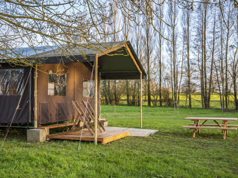 Outdoor-Glamping-Zelt mit Holzterrasse und Picknicktisch in grüner Landschaft in Pays de la Loire, Frankreich.