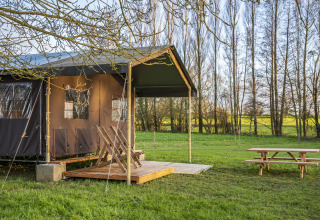 Outdoor-Glamping-Zelt mit Holzterrasse und Picknicktisch in grüner Landschaft in Pays de la Loire, Frankreich.