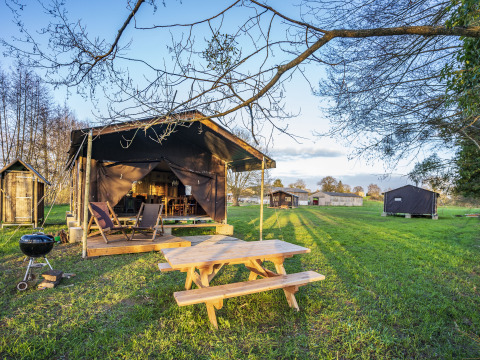 Glamping-telt med træmøbler og grill i grønne omgivelser på BoerenBed L'Étable des Mauges en Anjou, Frankrig.