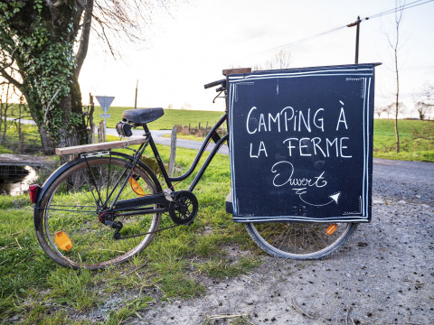 Bicicletta con cartello 'Camping à la ferme ouvert' accanto a una strada in Pays de la Loire, Francia.