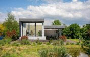 Moderne Boslodge Plus med store vinduer og terrasse omgivet af grøn natur i 't Schuttenbelt, Holland.