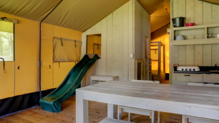 Innenaufnahme eines Safari-Zeltes mit Rutsche, Esstisch und Küche im Family Park Goolderheide, Belgien.