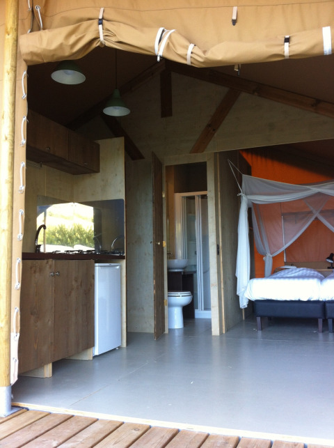 Interieur van een safaritent op Camping Podere sei Poorte in Italië, met keuken, bed en badkamer.