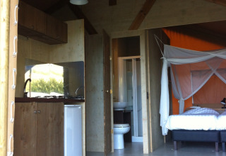 Interieur van een safaritent op Camping Podere sei Poorte in Italië, met keuken, bed en badkamer.