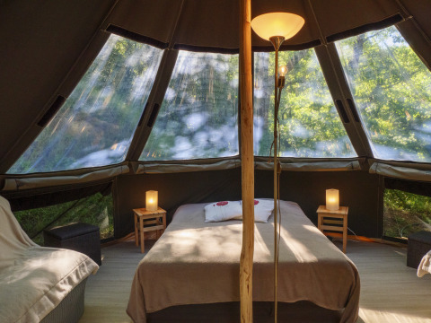 Interieur van de Inuit Forest Tent op Campsite Des Randonneurs in Frankrijk, met bed, lampen en boszicht.