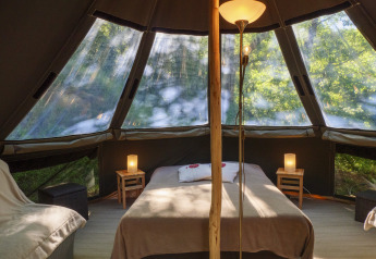 Interior of the Inuit Forest Tent at Campsite Des Randonneurs, France, featuring bed, lamps, and forest views.