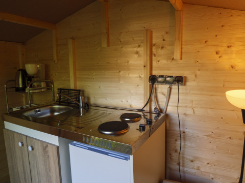 Piccolo angolo cottura con lavello, piastre, mini frigo e caffettiera in una tenda safari in legno.
