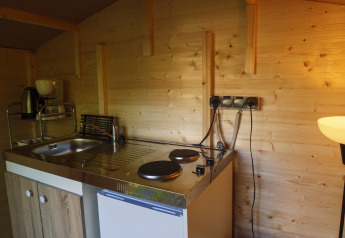 Small kitchenette with sink, hotplates, mini fridge and coffee maker inside a wood-paneled safari tent.