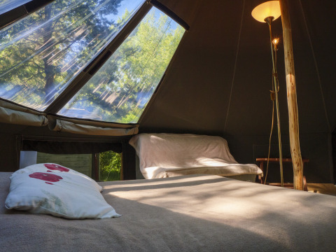 Binnenzijde van de Inuit Forest Tent op Campsite Des Randonneurs in Frankrijk met bed, bank en lichtkoepel.