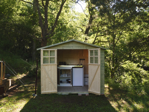 Houten schuurtje met open deuren, keukentje en mini-koelkast in het bos bij Campsite Des Randonneurs, Frankrijk