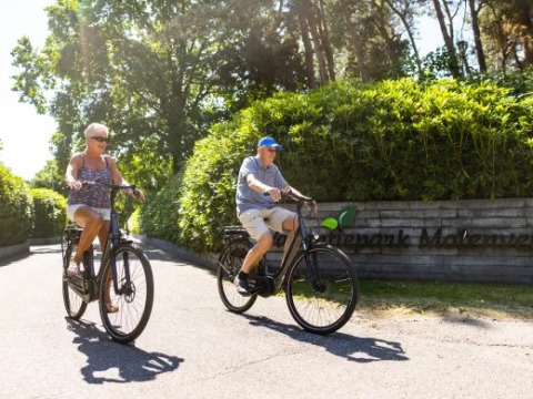 Due anziani in bicicletta al Holiday park Molenvelden, parco vacanze nel Brabante Settentrionale, Paesi Bassi.