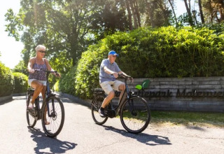 Dos personas mayores pasean en bicicleta por Holiday park Molenvelden, parque vacacional en Noord-Brabant, Países Bajos.