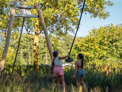 To børn leger på en gyngestativ blandt grønne træer i ferieparken Molenvelden, Noord-Brabant, Holland.