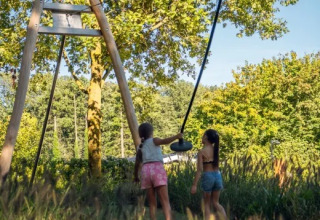 Due bambini giocano su un’altalena tra il verde al parco vacanze Molenvelden, Brabante settentrionale, Paesi Bassi.