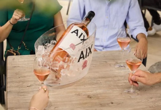 Tre persone gustano vino rosé a un tavolo con una grande bottiglia AIX nel ghiaccio al parco Molenvelden.