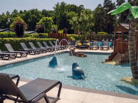 Udendørs swimmingpoolområde med solsenge, vandsprøjt og legeplads i ferieparken Molenvelden, Nordbrabant.