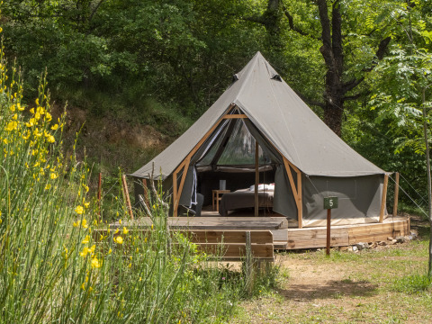 De Inuit Forest Tent safaritent staat op een houten platform in het bos, omgeven door bomen en bloemen.
