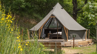 La tenda safari Inuit Forest Tent si trova su una pedana di legno nella foresta, circondata da alberi e fiori.