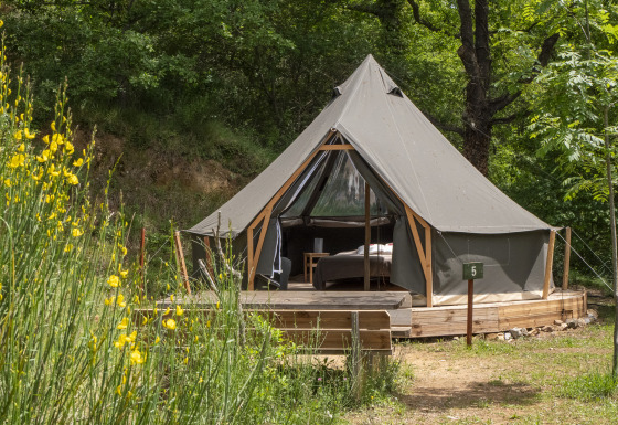 La tenda safari Inuit Forest Tent si trova su una pedana di legno nella foresta, circondata da alberi e fiori.