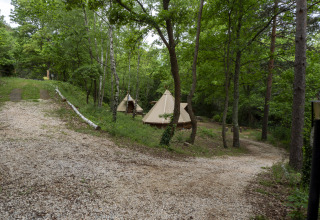 Grindpad naast het Modern Tipi bij Camping Des Randonneurs in Frankrijk, omgeven door groene bomen.