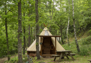 Modern Tipi-tent bij Campsite Des Randonneurs in Frankrijk, omgeven door groen bos en picknicktafel.