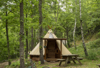 Modern Tipi tent at Campsite Des Randonneurs in France, surrounded by lush green forest and picnic table.