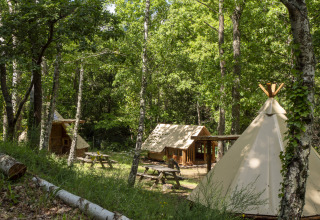 Tipi moderni al Campeggio Des Randonneurs in Francia, immersi nel verde bosco con tavoli da picnic in legno.