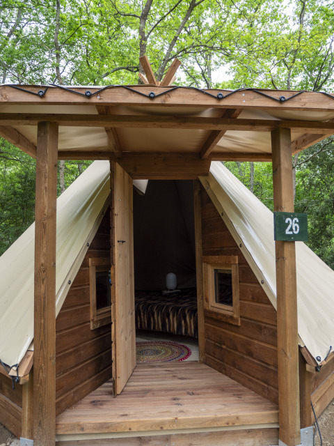 Modern tipi-tent met houten voorzijde en open deur op Campsite Des Randonneurs in Frankrijk, omringd door bomen.