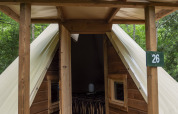 Modern tipi tent with wooden front and open door at Campsite Des Randonneurs in France, surrounded by trees.