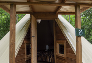 Modern tipi tent with wooden front and open door at Campsite Des Randonneurs in France, surrounded by trees.