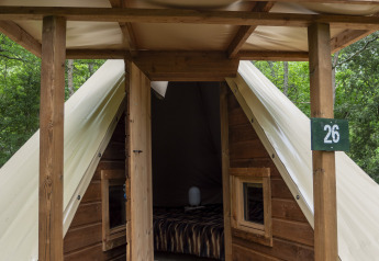 Modern tipi tent with wooden front and open door at Campsite Des Randonneurs in France, surrounded by trees.