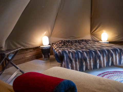 Interior of a modern tipi tent at Campsite Des Randonneurs in France, featuring bed, lamps, and cozy décor.