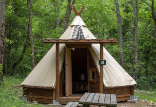 Modern tipi tent at Campsite Des Randonneurs in France, surrounded by trees with a picnic table outside.