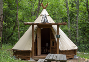 Modern tipi tent at Campsite Des Randonneurs in France, surrounded by trees with a picnic table outside.
