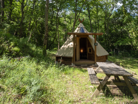 Modern tipi tent at Campsite Des Randonneurs in France, set in a wooded area with a picnic table.