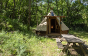 Modern tipi tent at Campsite Des Randonneurs in France, set in a wooded area with a picnic table.
