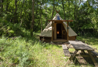 Modern tipi tent at Campsite Des Randonneurs in France, set in a wooded area with a picnic table.