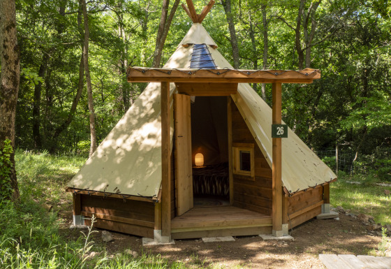 Modern tipi-tent in het bos met houten structuur en open deur die een gezellige binnenkant toont.