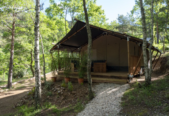 Safari Lodge tent nestled in a lush green forest, surrounded by trees and a gravel path leading to porch.