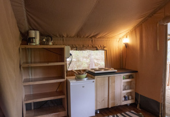 Kitchen area inside a safari tent at Safari Lodge, Campsite Des Randonneurs, France, with shelves and small fridge.