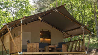 Safari Lodge LUXE telt med sanitære faciliteter, træterrasse og siddeområde, omgivet af grøn skov.