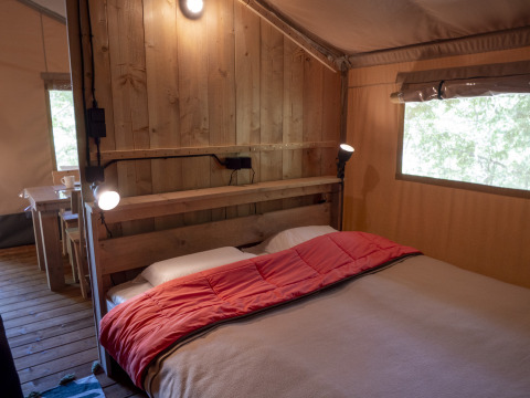 Slaapkamer in Safari Lodge LUXE tent op Camping Des Randonneurs in Frankrijk, met bed en houten muur.