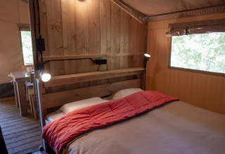 Camera da letto nella Safari Lodge LUXE al Campeggio Des Randonneurs in Francia, con letto e pareti in legno.