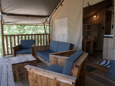 Overdekte zithoek in de Safari Lodge LUXE tent met houten meubilair op Camping Des Randonneurs, Frankrijk.