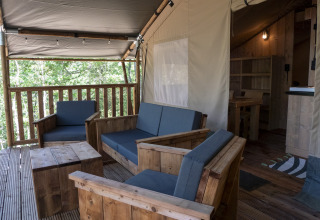 Overdekte zithoek in de Safari Lodge LUXE tent met houten meubilair op Camping Des Randonneurs, Frankrijk.