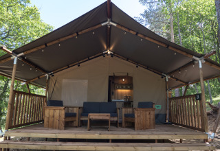Safari Lodge LUXE tent op Camping Des Randonneurs in Frankrijk met houten veranda en zithoek buiten.