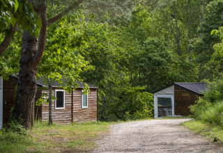 Schotterweg vor Mobile Home Tithome auf dem Campingplatz Des Randonneurs, umgeben von grünen Bäumen.